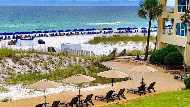 Ein Hotel direkt am Strand mit Liegestühlen und Sonnenschirmen, einem Sandstrand und Blick aufs Meer.