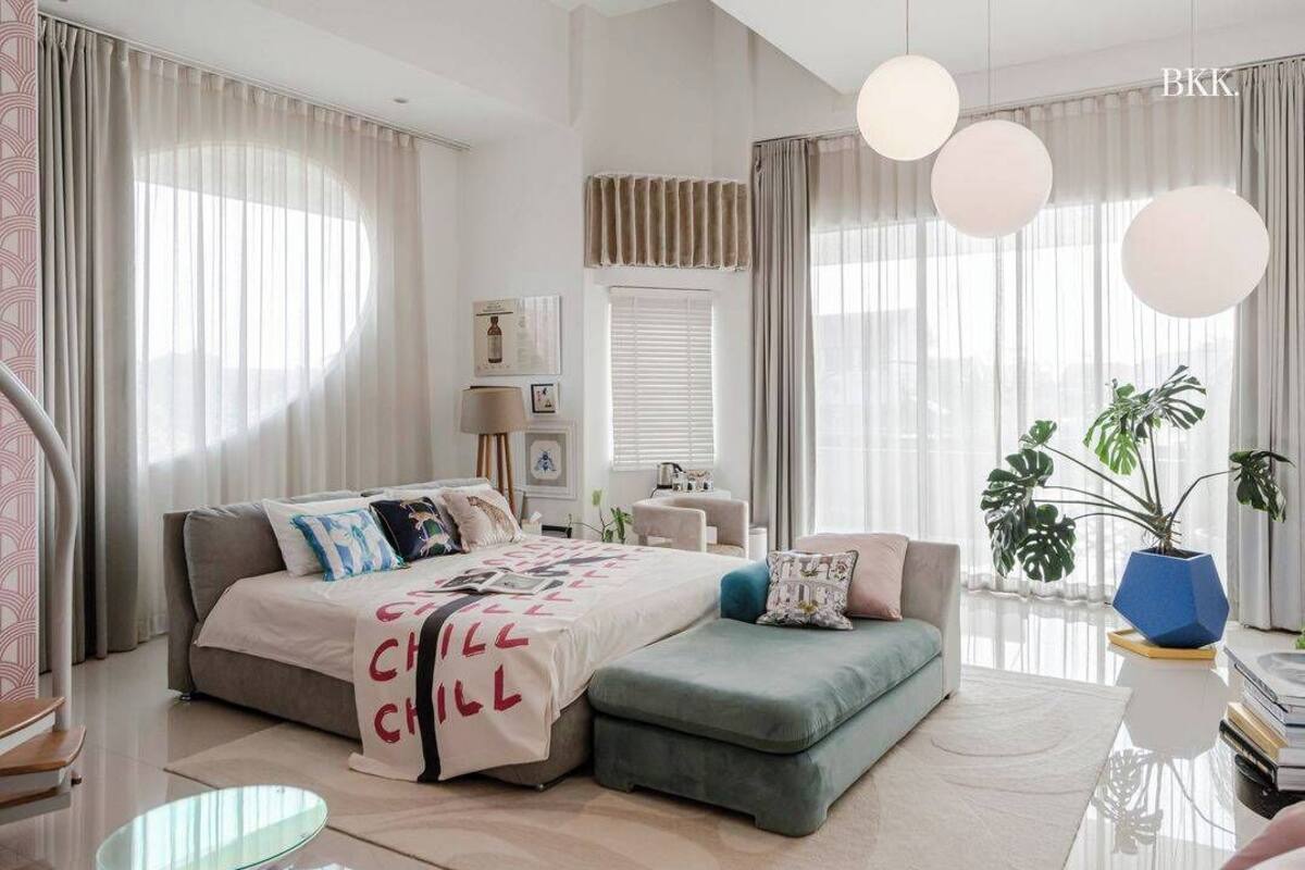 A modern bedroom with a bed, bedside tables, a desk, a chair, a potted plant, and a large window with curtains.