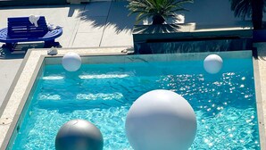 A swimming pool with clear water, a person holding large white balls, and a blue bench. - CASA PAPA Home&Space (Nakhon Chai Si)