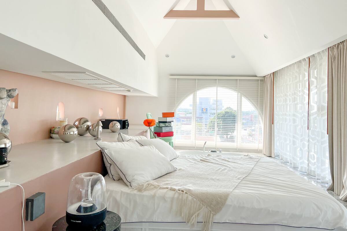 A modern bedroom with a bed, bedside table, lamp, and a view of the city through large windows.
