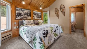 Una camera da letto con un letto, soffitto in legno, due quadri appesi al muro e una porta che dà su un'altra stanza.