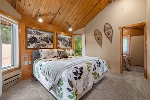 A bedroom with a bed, wooden ceiling, two wall-mounted pictures, and a door leading to another room.