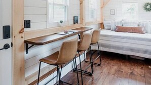 A room with a wooden ceiling, a bed with pillows, a desk with chairs, and a window. - Tiny Timber- Stunning Tiny House (Spearfish)