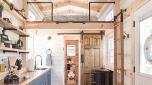 A kitchen with wooden beams, a central island, and a view to the dining area. - Tiny Timber- Stunning Tiny House (Spearfish)