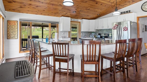 Una cucina con soffitto in legno, mobili bianchi, elettrodomestici in acciaio inox e un'area bar con sedie in legno.