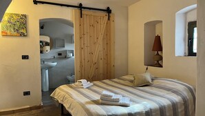 Una camera da letto con un letto, un armadio in legno, un bagno con lavandino e bidet e un quadro appeso al muro.