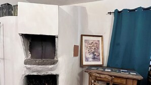 Una stanza d'angolo con camino, una sedia di legno, un tavolo con un portafoto e una tenda blu.