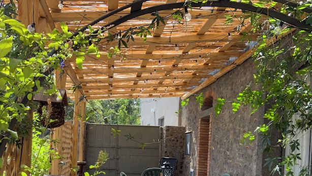 Un patio con una pergola in legno, posti a sedere all'aperto e un muro in pietra.