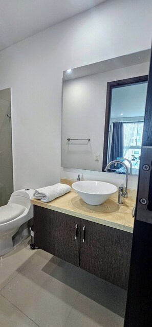 Ein modernes Badezimmer mit Toilette, einem großen Waschbecken und einem Spiegel darüber.