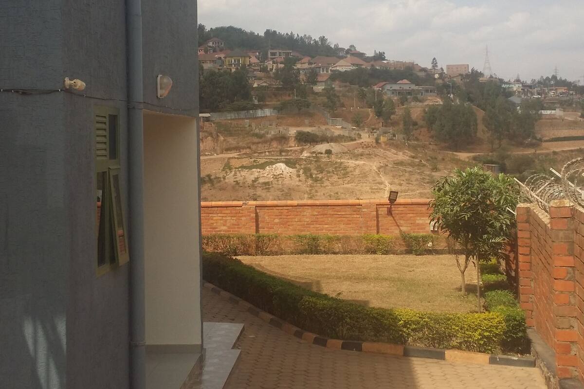 A paved walkway leading to a building with a view of a hilly landscape in the background.