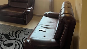 Ein Wohnzimmer mit zwei Ledersofas, einem gemusterten Teppich, einem Deckenventilator und einem Fenster mit schmiedeeisernen Gitterstäben.
