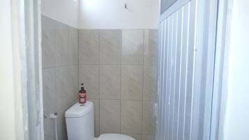 Un baño pequeño con azulejos, un inodoro y una botella de Jabón Puerta Roja.