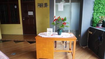 Una mesa de madera con un mantel individual, un código QR y una maceta con flores rojas.