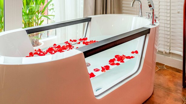 A modern bathroom with a large bathtub, a glass-enclosed shower, and a view of greenery outside. - Mai Hotel  (Hanoi)