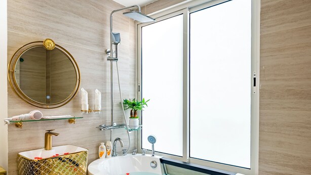 A modern bathroom with a freestanding bathtub, a large mirror, and a window providing natural light. - Mai Hotel  (Hanoi)