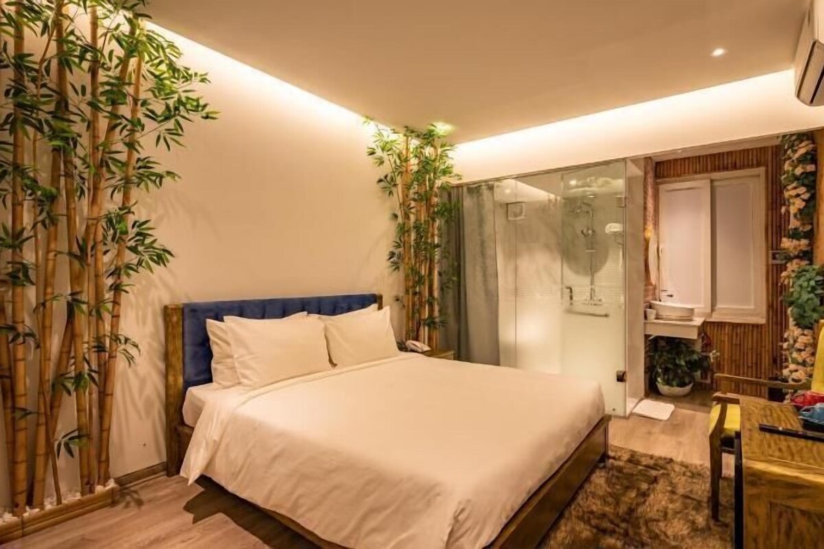 A bedroom with a bed, a glass shower, a TV, and a bamboo wall.