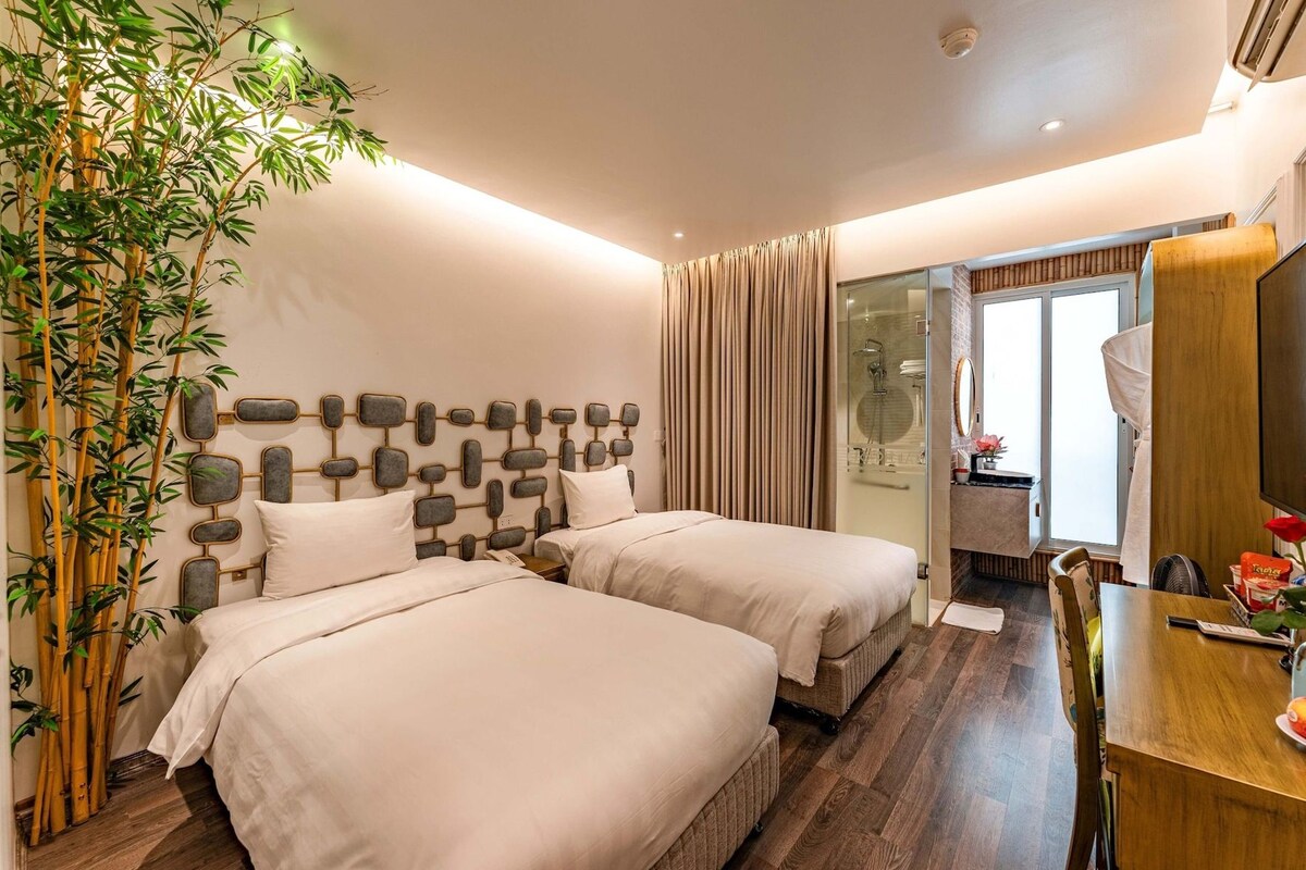 A hotel room with two beds, a large mirror, a wooden dining table, and a bamboo plant.
