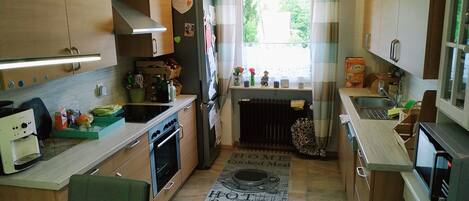 Een compacte keuken met houten kastjes, een fornuis, een spoelbak en een raam met gordijnen.