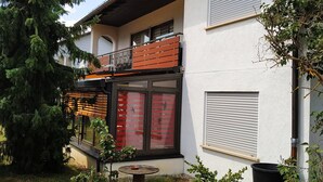 Ein Gebäude mit Balkon, einem Fenster mit rotem Rollo und einem kleinen Tisch mit einer Schale.