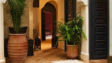 A pool area with a tiled edge, a large potted plant, and a doorway leading to a room with a red carpet.