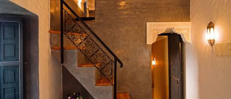 A staircase with a wrought iron railing, a door with a decorative arch, and wall-mounted lighting.