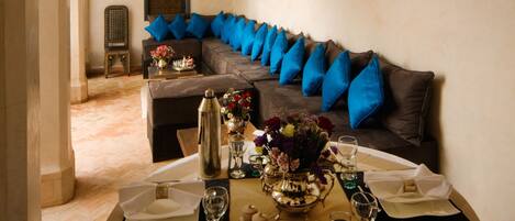 Un comedor con una mesa dispuesta para cuatro personas, un sofá con cojines azules y un panel decorativo en la pared.