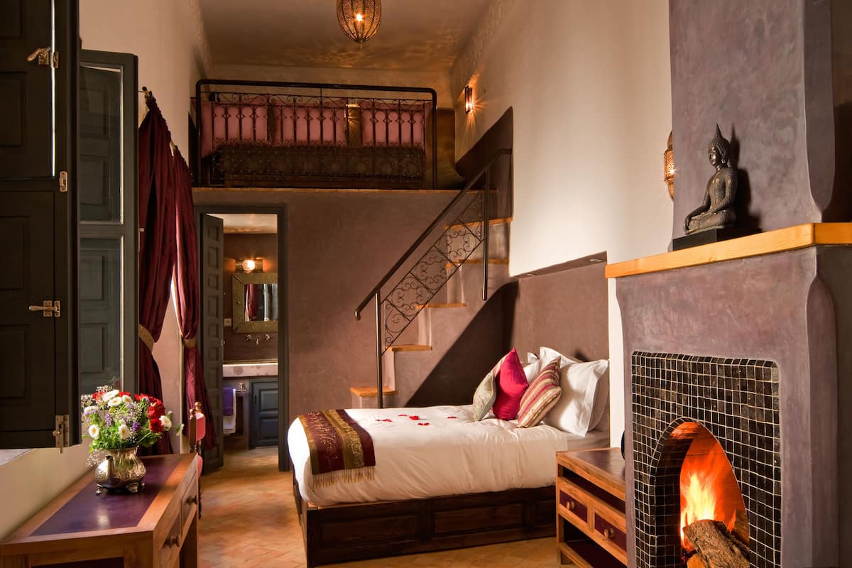 A bedroom with a bed, a fireplace, a staircase, and a decorative statue.