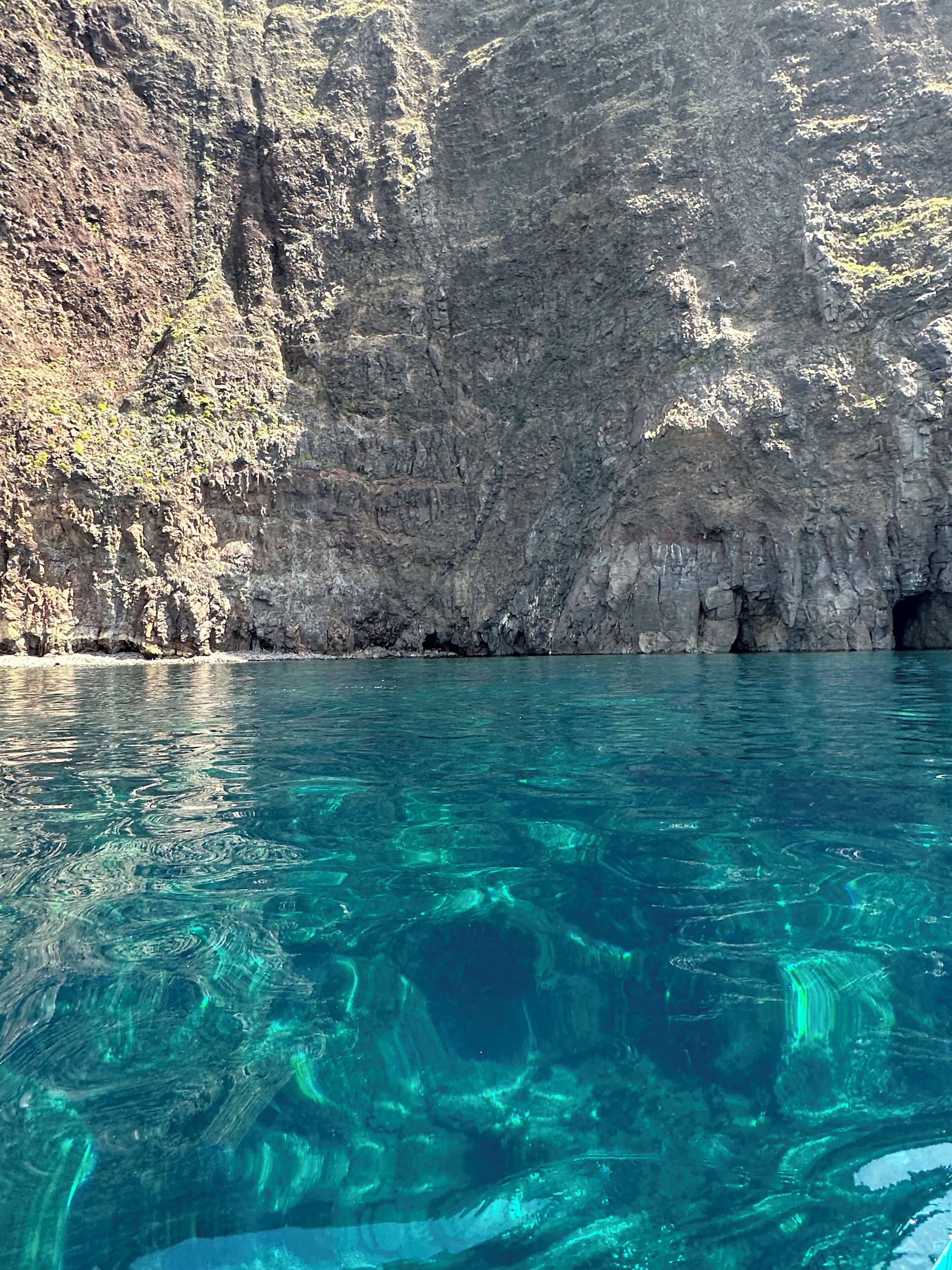 A clear blue sea with rocky cliffs in the background.
