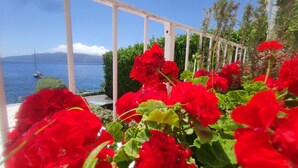 Varanda com flores vermelhas e vista para o mar e montanhas.