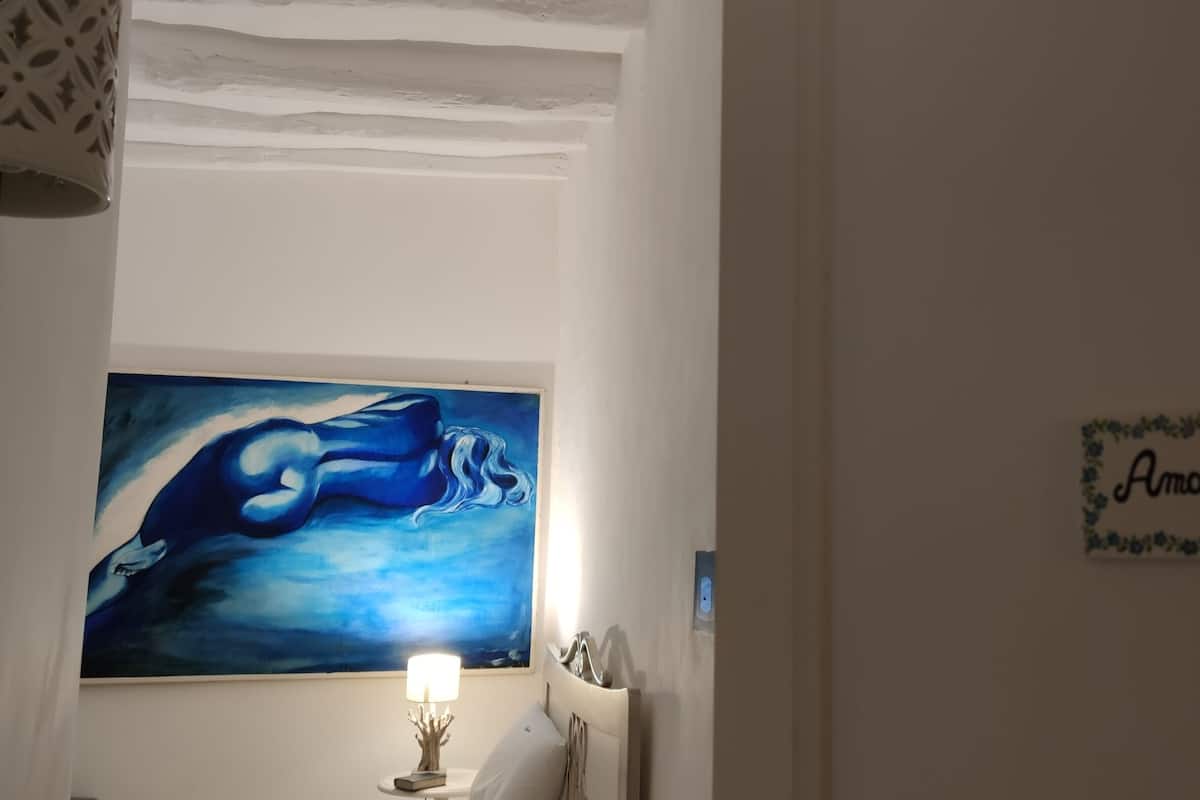 Et værelse med et maleri af en hval på væggen, et sengebord med en lampe, og et indrammet skilt med navnet 'Amarea'.