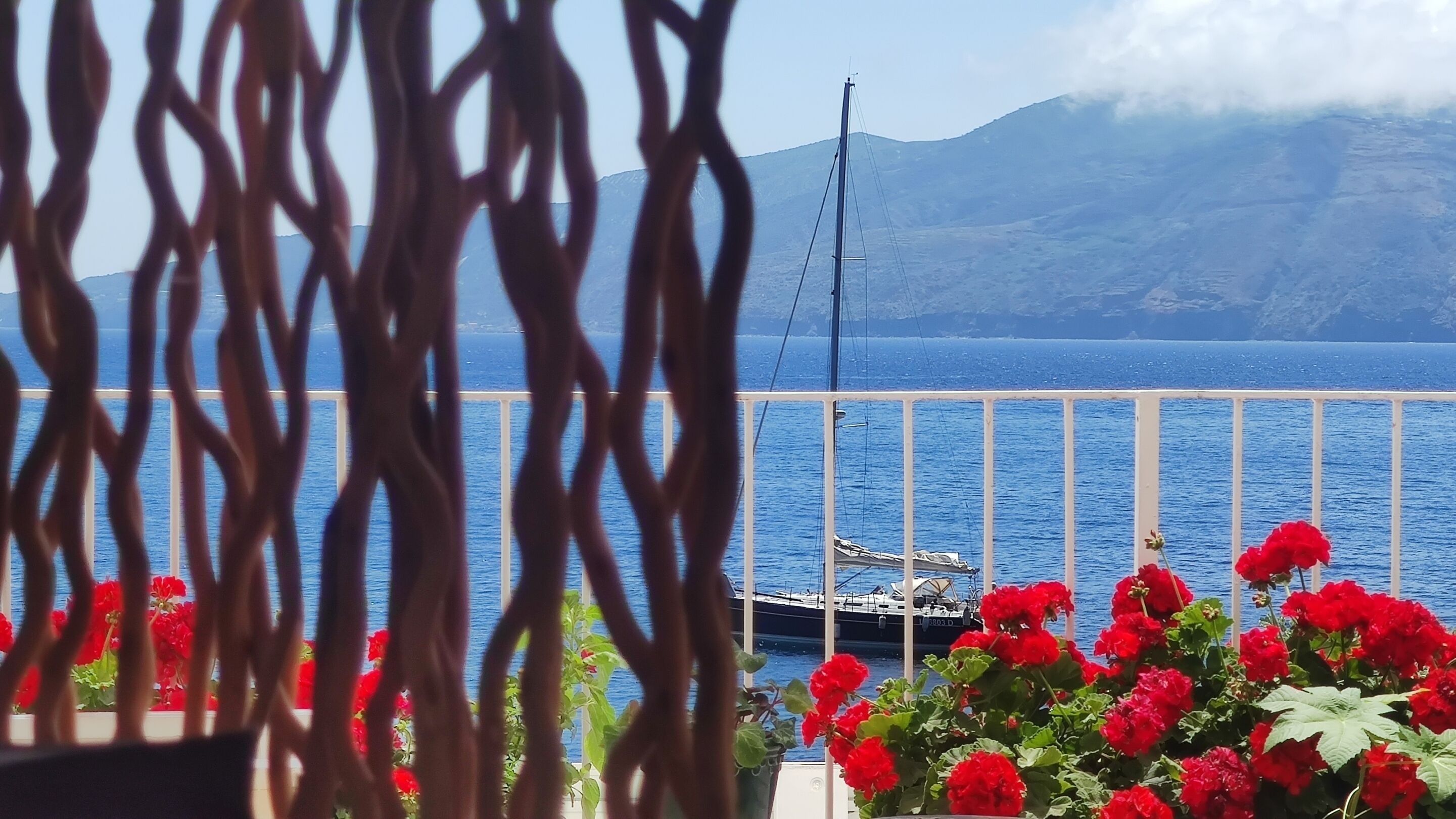 Ein Balkon mit Blick auf ein Gewässer, ein Boot und Berge im Hintergrund.