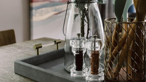 Un plan de travail de cuisine avec un vase en verre contenant des plantes vertes, un étagère à épices et un porte-ustensiles.
