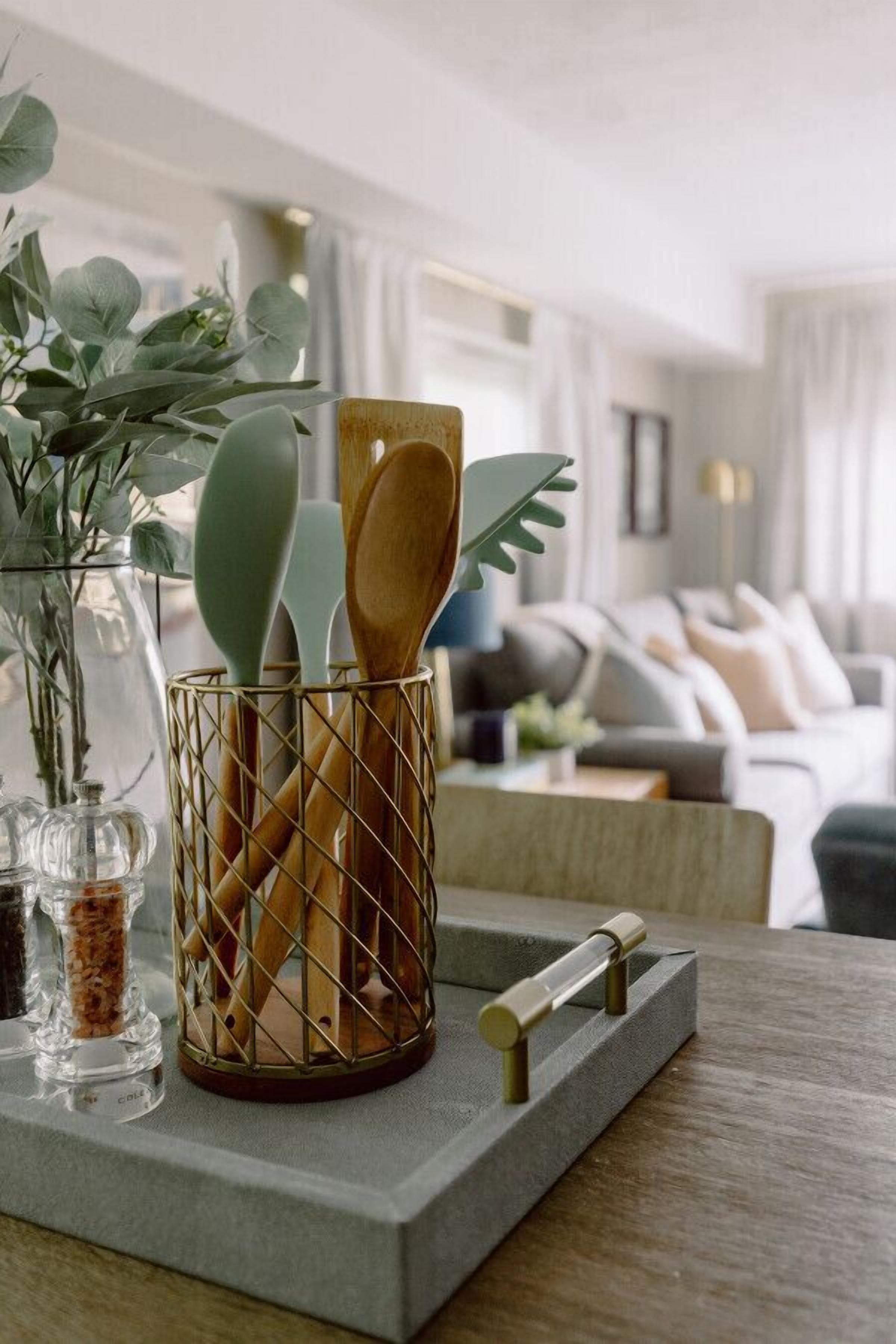 Een keukentafel met een houten messenhouder, een glazen pot met kruiden en een plant op de achtergrond.