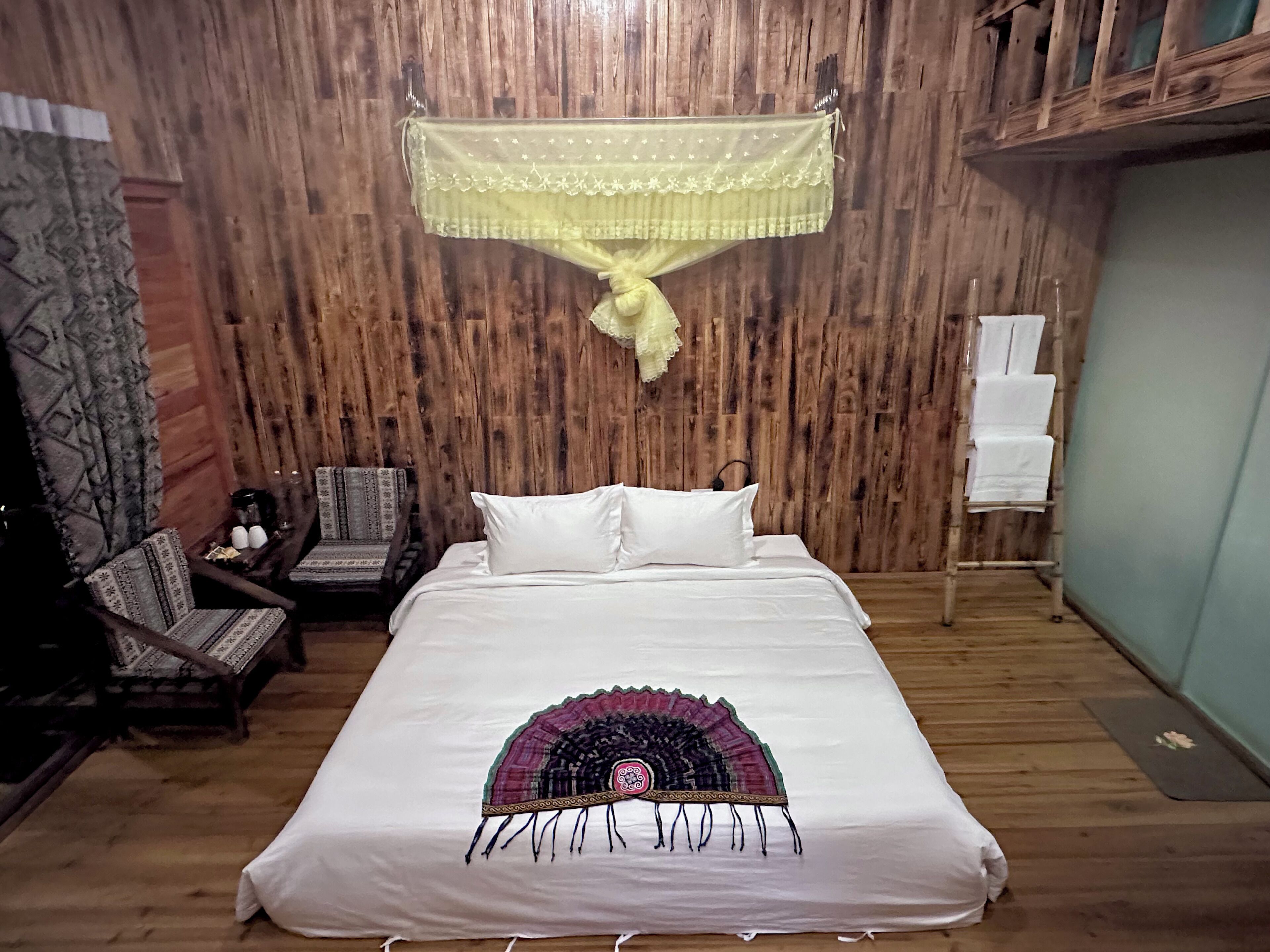 Un dormitorio con pared de madera, una cama con almohada decorativa, una silla y una mesita.
