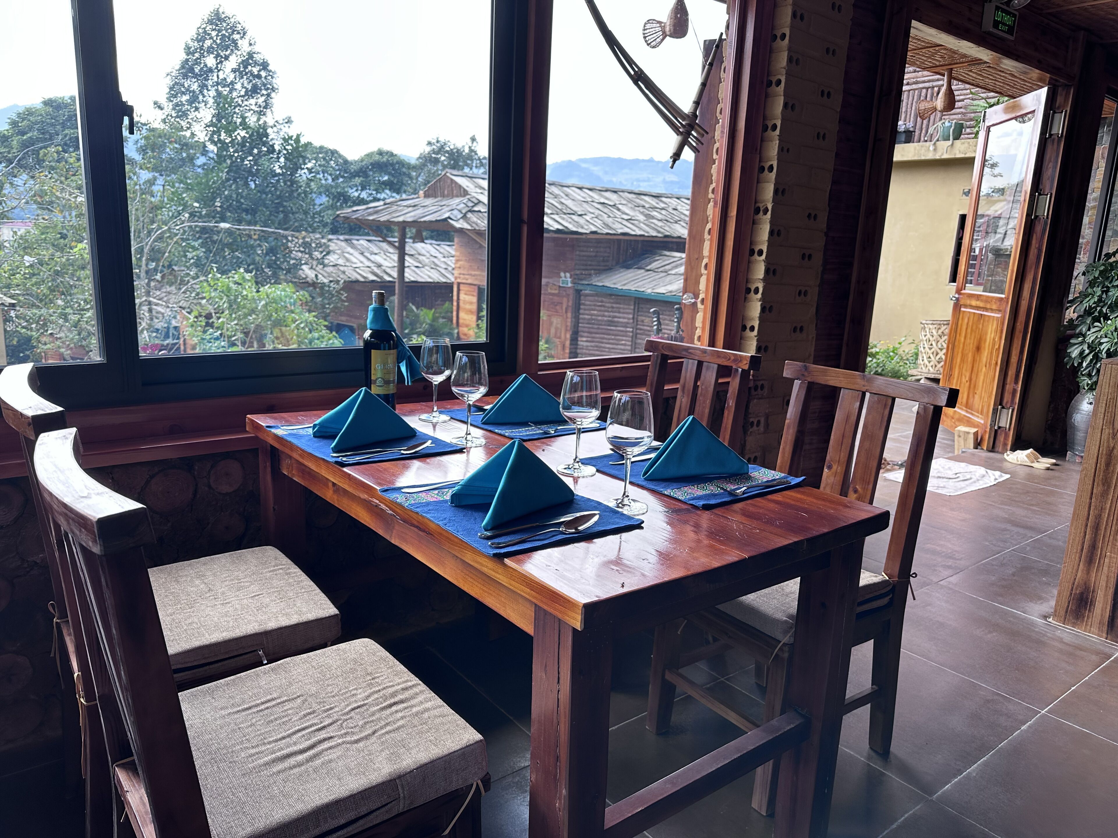Un comedor con una mesa de madera dispuesta para cuatro, servilletas azules y una botella de vino.