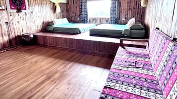 A wooden cabin bedroom with two beds, a bench, and a patterned bench seat.