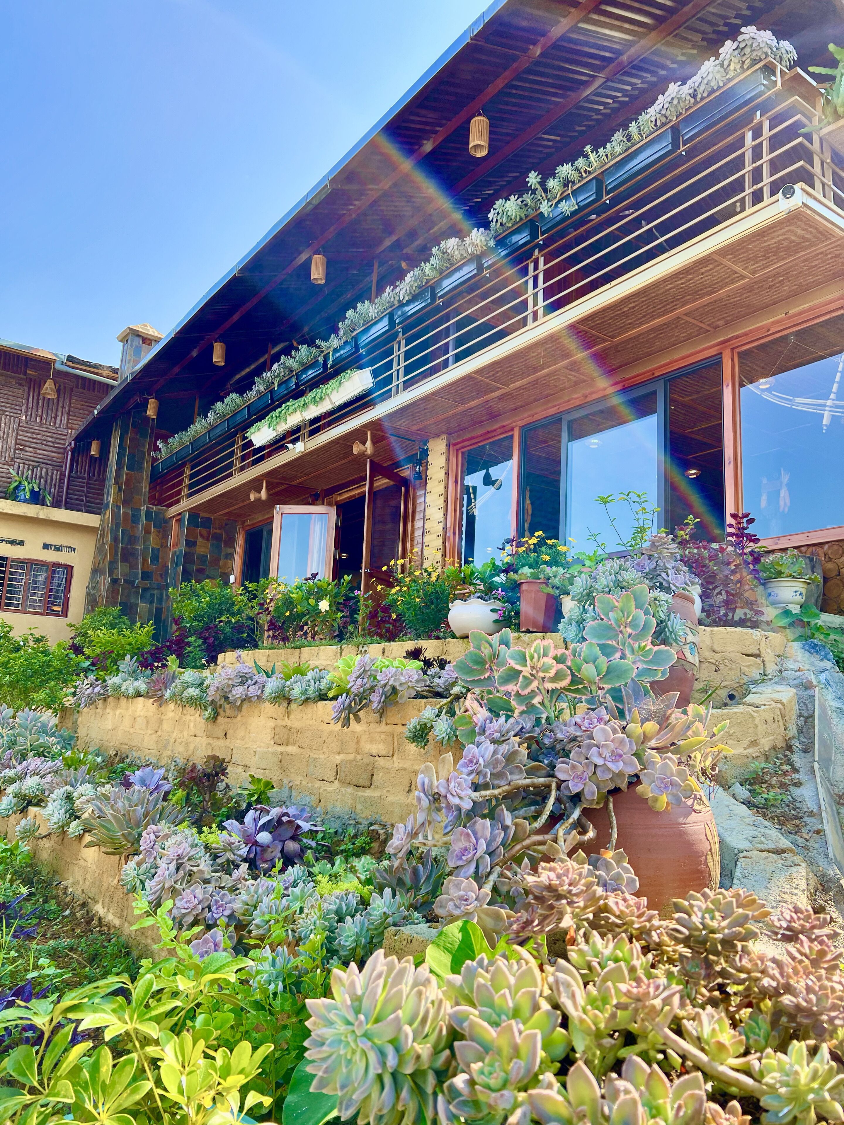 A two-story building with a balcony, potted plants, and a stone wall.