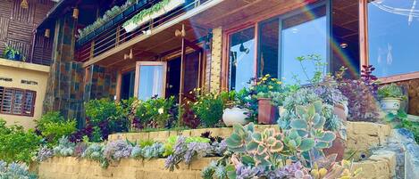 A two-story building with a balcony, potted plants, and a stone wall.