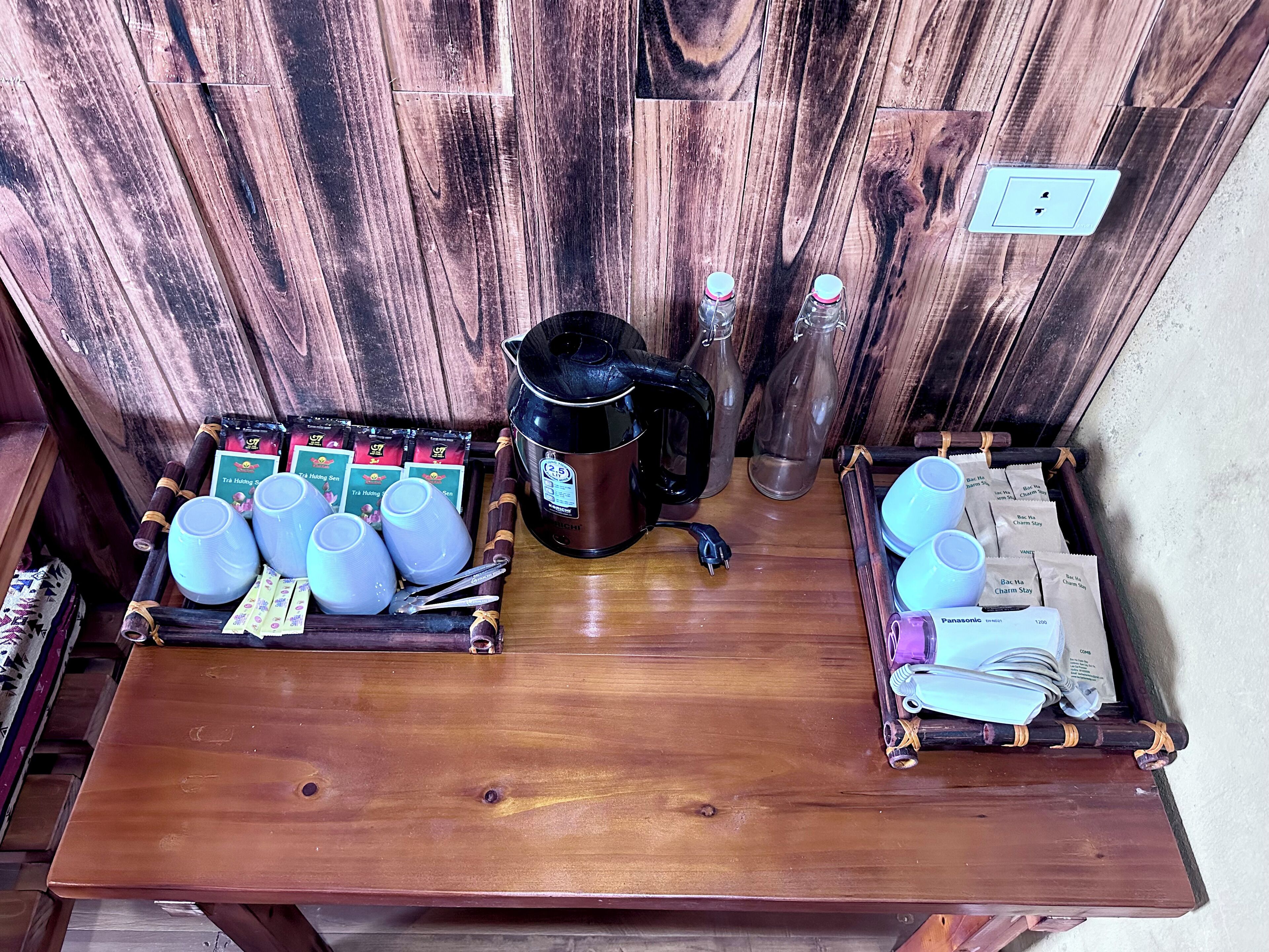 Une table en bois avec une machine à café, des théières, des tasses et des sachets de thé.