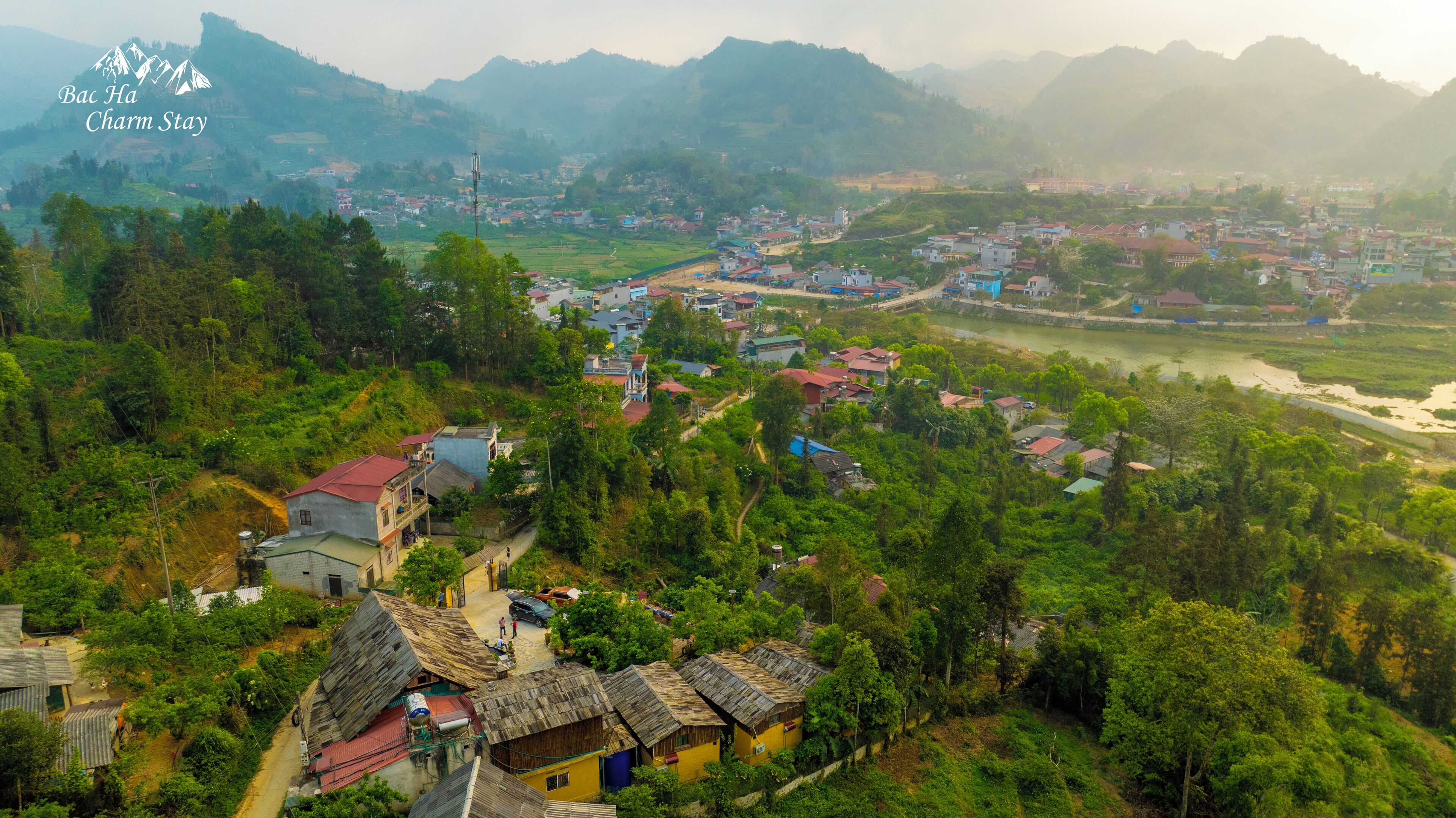 A rural village with traditional houses, a river, and mountains in the background.