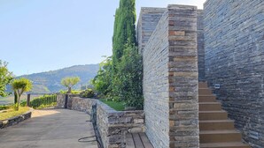 A stone staircase leading up to a building with a stone facade, surrounded by greenery and a view of hills.