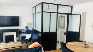 Un salon moderne avec un téléviseur, un fauteuil bleu, une table basse en bois et une cloison noire avec des panneaux de verre.