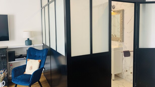 Une chambre moderne avec un fauteuil bleu, un téléviseur et une cloison en verre à cadre noir.
