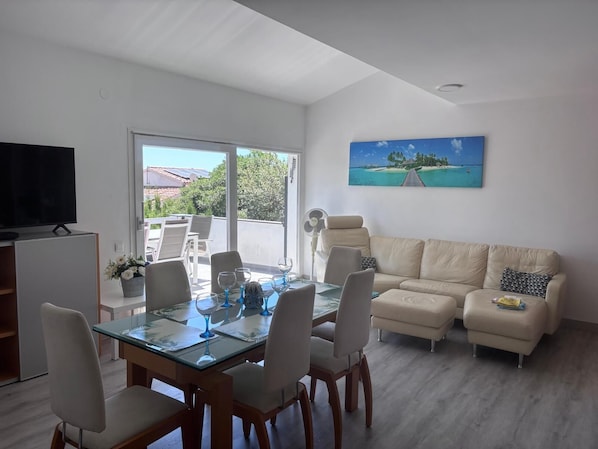 Un coin repas avec une table en verre, des chaises et un téléviseur.