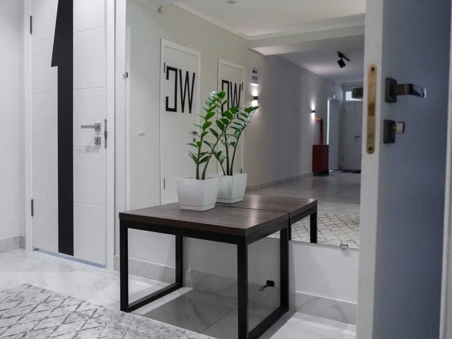 A modern hallway with white walls, a marble floor, and a table with potted plants.