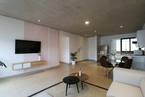 A modern living room with a flat-screen TV, a sofa, a coffee table, and a dining area with chairs and a kitchen in the background. - w* | Picturesque 2BR with Balcony in Miraflores (Miraflores)