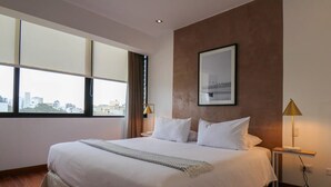 A modern hotel room with a large bed, a city view, and a framed picture on the wall. - w* | Picturesque 2BR with Balcony in Miraflores (Miraflores)
