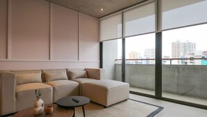 A modern living room with a sectional sofa, a small round table, and a large window offering a city view. - w* | Picturesque 2BR with Balcony in Miraflores (Miraflores)