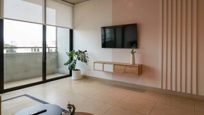 A modern living room with a large sliding glass door, a flat-screen TV mounted on the wall, a wooden console table, and a potted plant. - w* | Picturesque 2BR with Balcony in Miraflores (Miraflores)
