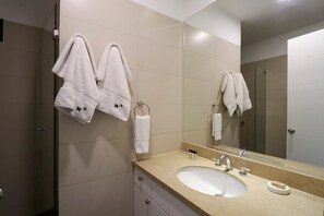 A modern bathroom with a beige tiled wall, a large mirror, a white sink, and two towels hanging on hooks. - w* | Picturesque 2BR with Balcony in Miraflores (Miraflores)